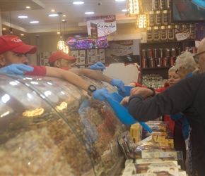 Lots of different selections of nuts. Behind 2 guys dressed in red offering tasters in blue shovels