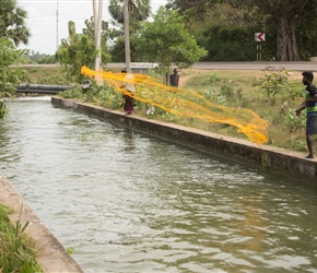 Fishing in the canal using a net that's weighted all around. Throw it in and catch the fish...