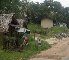 Sharon descends past a shop and milepost. This road was rough but all along there were signs of widening and an upgrade up coming. Sri Lanka do things not in halves, many kilometers are worked on by hundreds of road crew