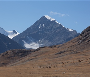 A mounted shepherd checks his flock in the shadow of the mountain